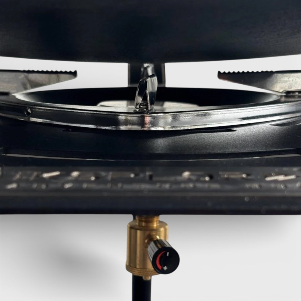 Close-up of a portable camping stove with a black top and brass control valve on a white background.